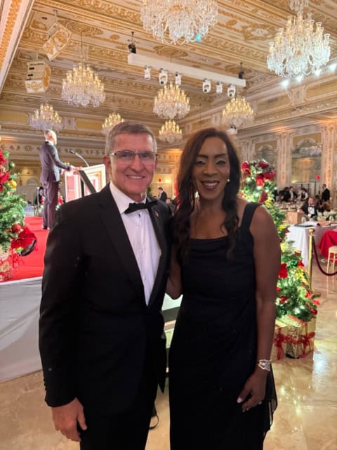 Bernadette Smith and a man at a formal event in an elegant, chandelier-lit ballroom decorated for th.