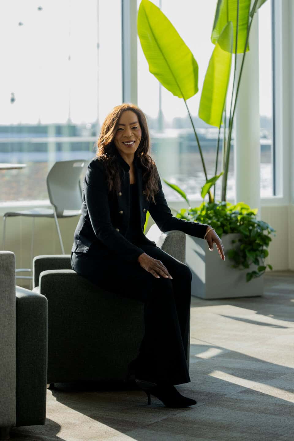 Empowered woman smiling, sitting in bright modern office with green plants, promoting Bernadette Smith for U.S. Senate.