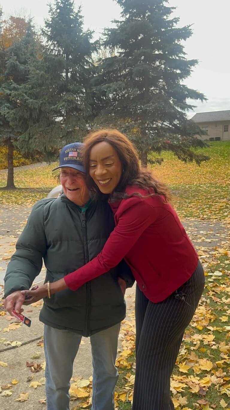 Veteran man smiling with a woman outdoors in fall, autumn leaves on ground, happy community gathering.