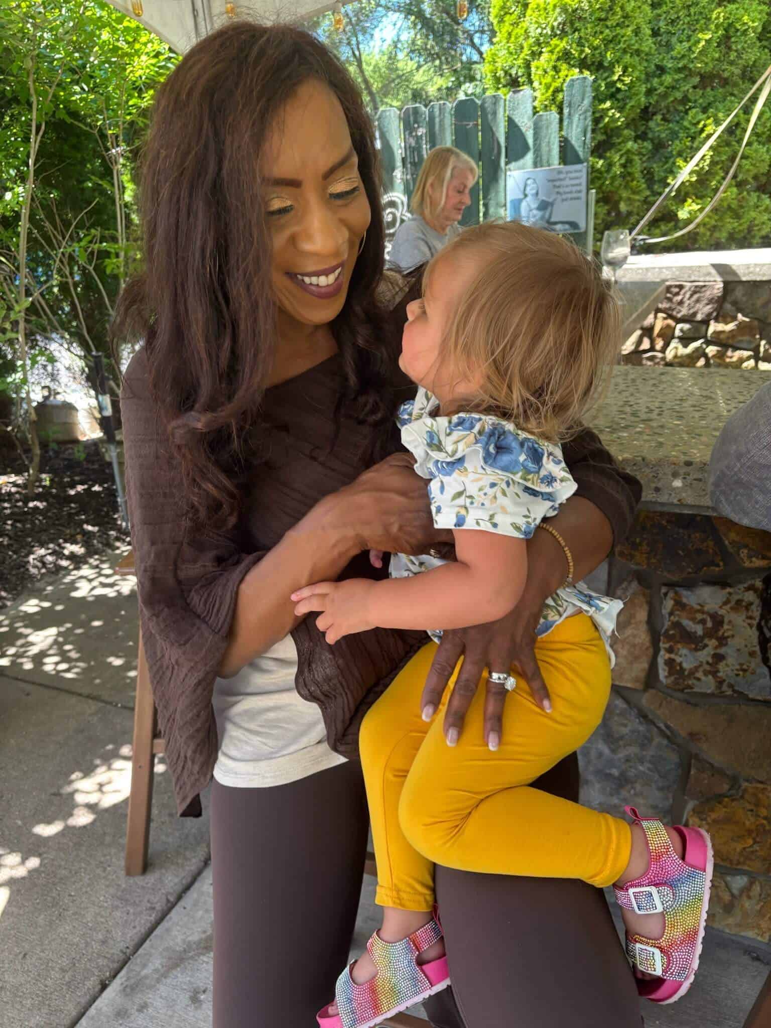 Happy woman holding a young girl outdoors at a social gathering.
