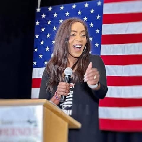 Bernadette Smith speaking at a campaign event with American flag backdrop.