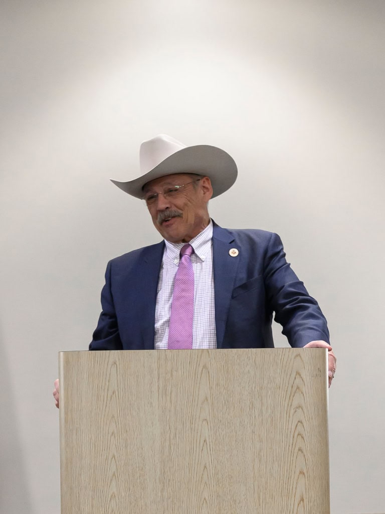 Bernadette Smith speaking at a campaign event, wearing a cowboy hat and suit.